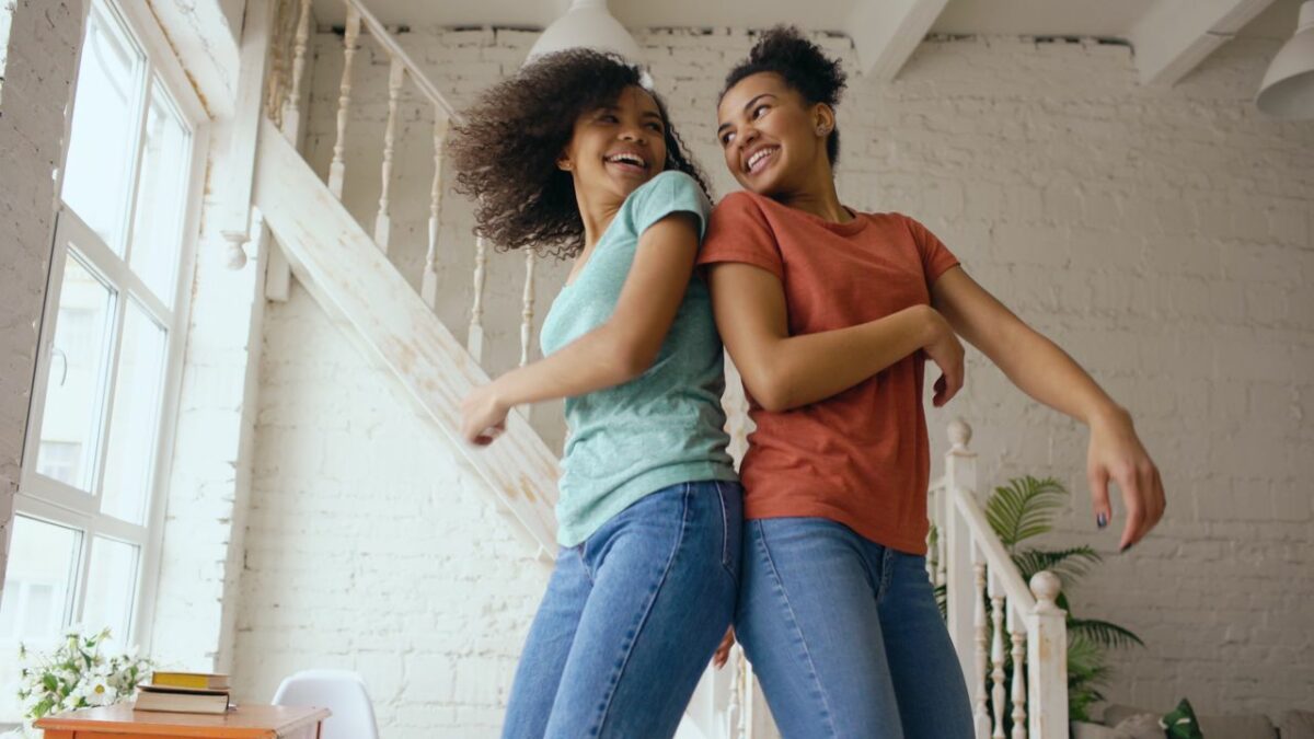 Twee vrouwen dansen met elkaar, met de ruggen bij elkaar kijken ze elkaar lachend aan