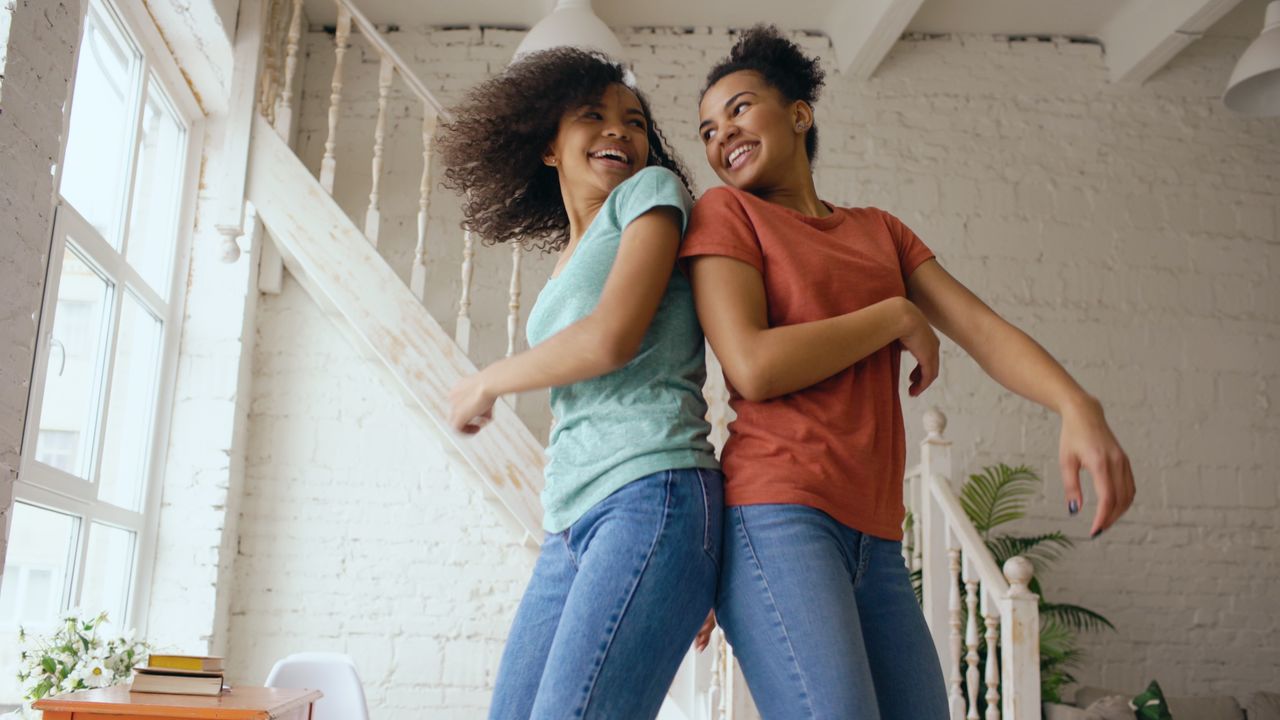 Twee vrouwen dansen met elkaar, met de ruggen bij elkaar kijken ze elkaar lachend aan